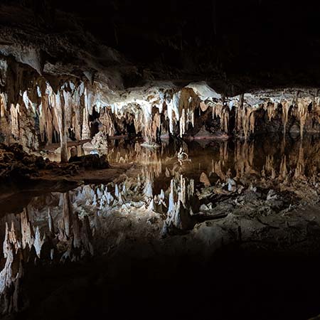 Photograph of a reflection pool within a cavern. The pool is a perfect mirror, reflecting the stalactites above so clearly that they could be mistaken for stalagmites below.