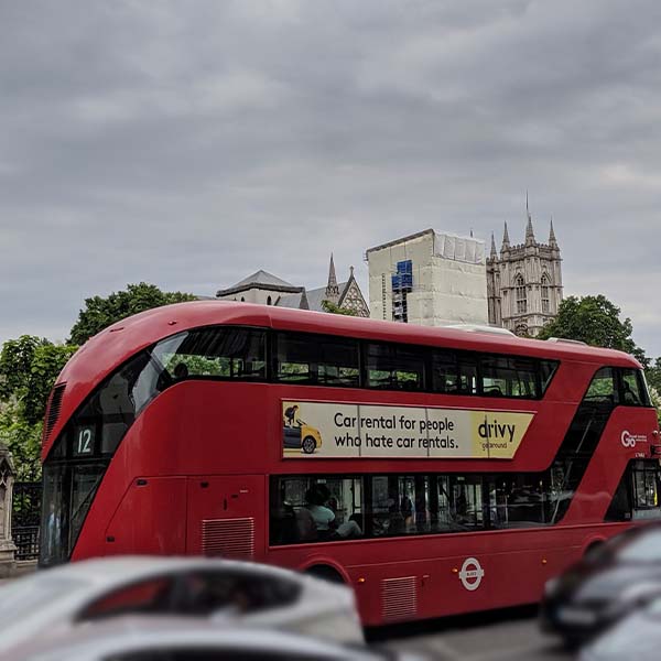 Photograph of a modern red double-decker bus in the middle of Westminster traffic. The top of the bus is curved, and the windows create horizontal lines across its body.