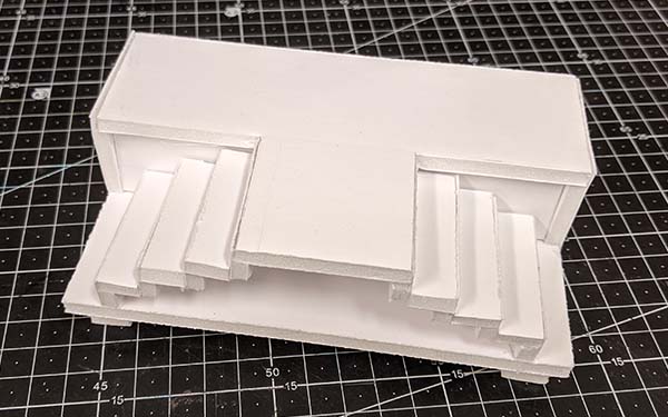 Side 1 of foam core table model A, the base is sealed and there are stairs on the right and left half of the table leading up to a “T” shaped tabletop.