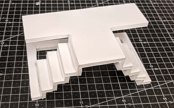 Side 1 of foam core table model B, the base is open below the two sets of stairs leading up to the “T” shaped table top.