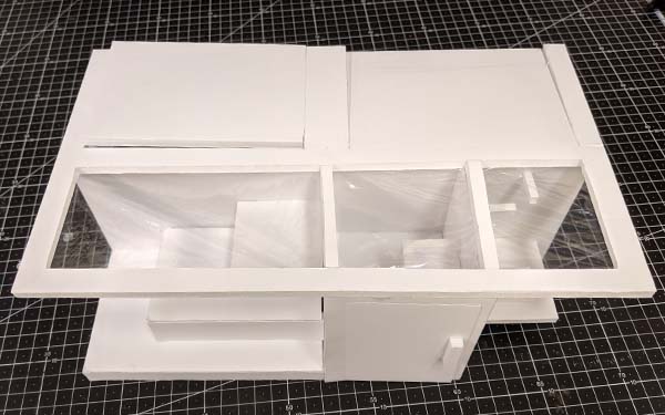 Side 1 of foam core table model I. The back portion of the table is solid, with lines demarking sections, and the front half is clear., The leftmost section has tiered levels, the middle sections has a door sealing access from the front, and the rightmost sections has an accessible level and some kind of mounts close to the bottom of the tabletop